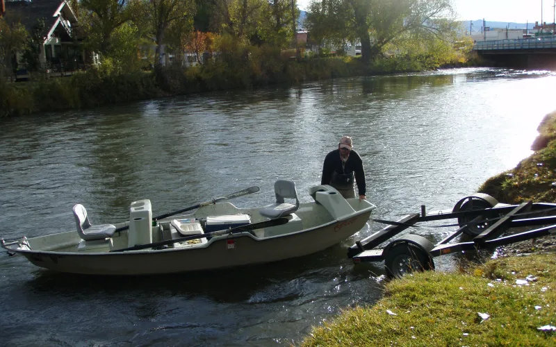 A man in waders launches a drift boat from its trailer into the Beaverhead River at Twin Bridges, Montana.