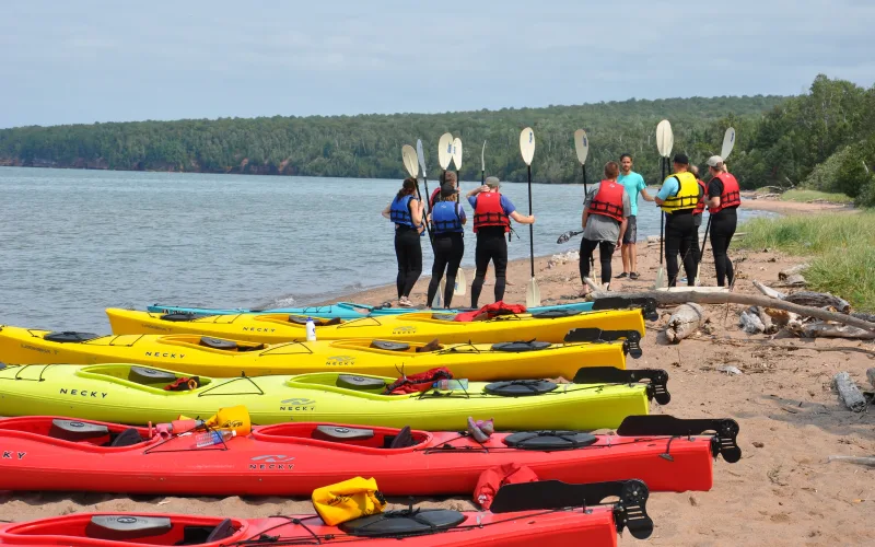 Sea kayakers in life jackets holding paddles stand in a circle on a Lake Superior beach for a safety talk before paddling to the sea caves at Apostle Islands National Lakeshore, Wisconsin