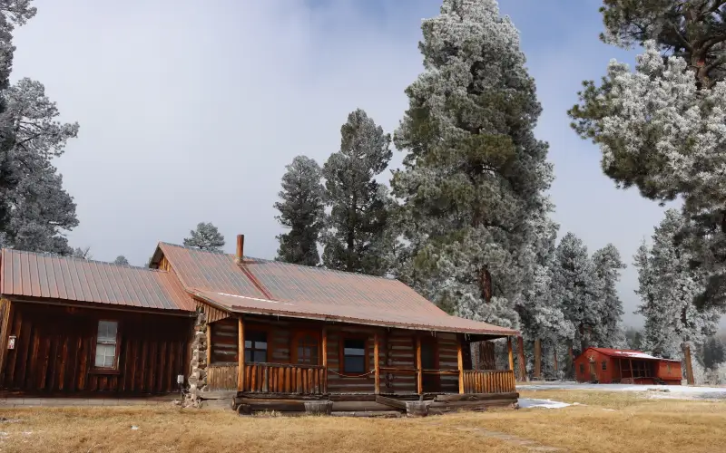 A historic log ranch foreman's cabin and a small red caretaker's cabin under frost-covered pines at Valles Caldera National Preserve, New Mexico
